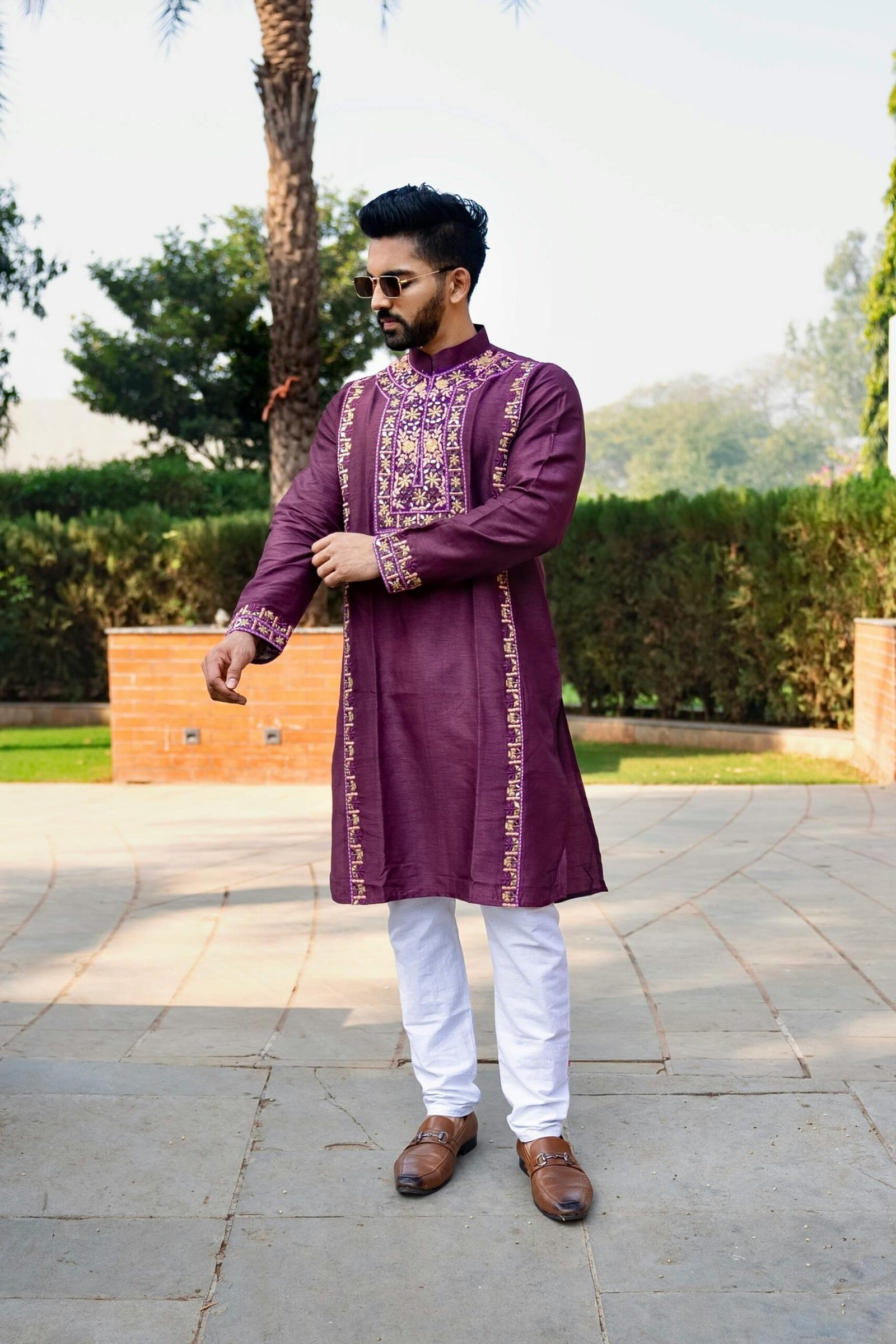 A fashionable man wearing a maroon kurta with intricate embroidery stands confidently outdoors in Ahmedabad, India.